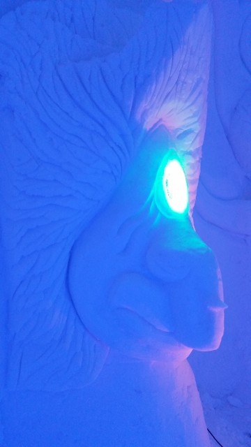 Abstract ice sculpture face illuminated with a vivid neon blue eye light