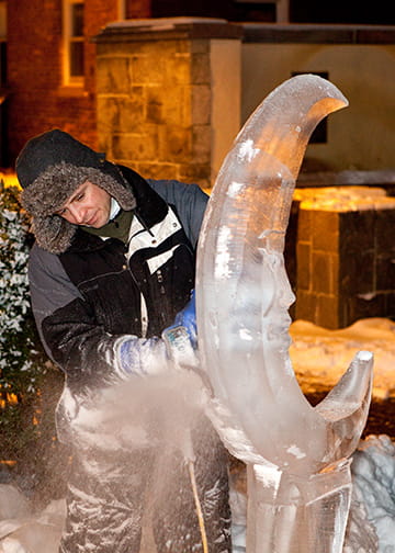 Ice carver under warm lighting working on a smooth curved ice installation
