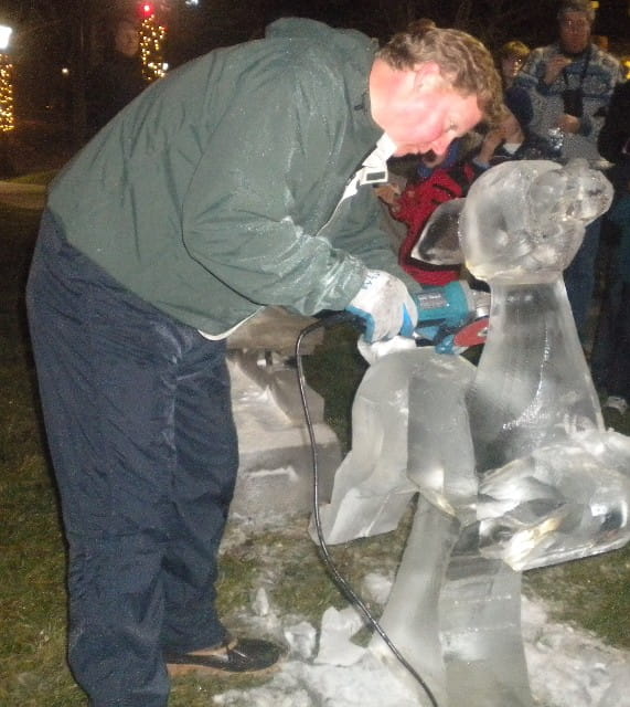 Sculptor bending down to carve fine details onto a public ice structure