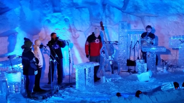 Acoustic band musicians playing live instruments inside a glowing blue winter ice cave
