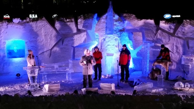 Crowd gathering at night in front of a giant multi colored illuminated ice castle wall