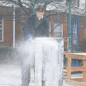 Ice carver operating a power tool creating ice mist on an outdoor display