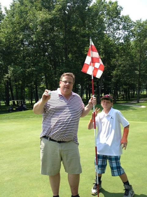 Two golfers posing happily on a sunny green golf course next to a flag