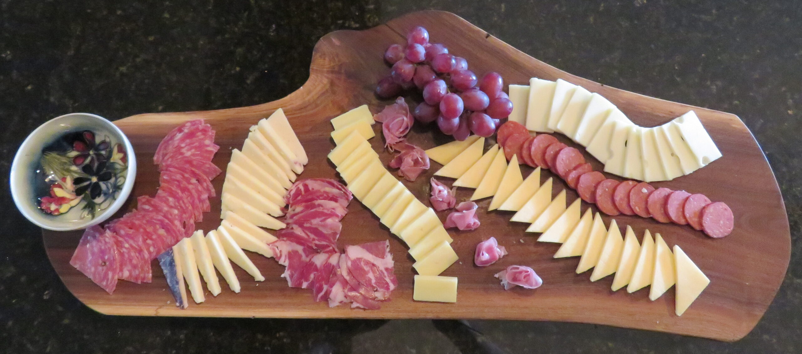 Catered gourmet charcuterie board arrangement featuring cheeses, crackers, and purple grapes