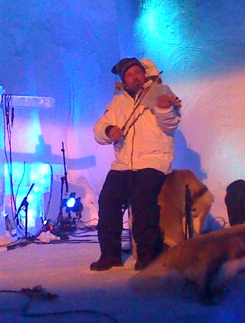 Performer on an outdoor winter stage entertaining a crowd near ice sculptures