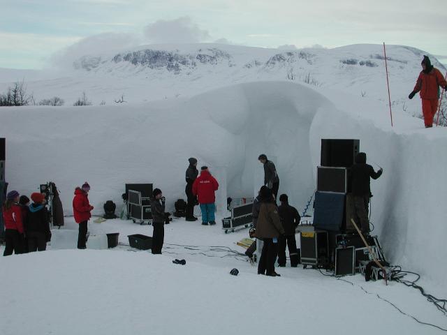 Crowd gathering around outdoor snow structures and an ice carving stage