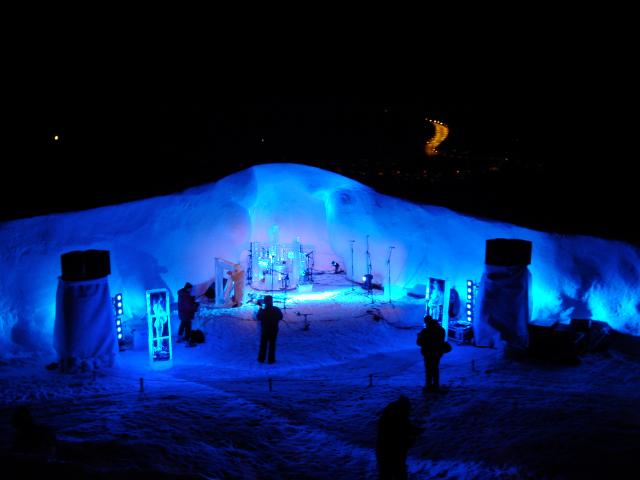 Wide view of an outdoor winter festival ice rink or lounge area lit in blue