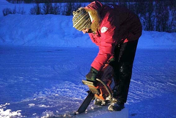 Person in a red jacket adjusting an outdoor ice blocks display in the snow