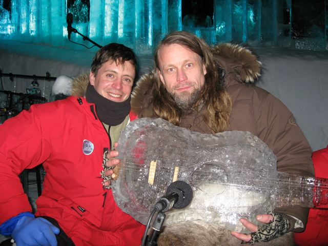 Two ice sculptors in winter jackets smiling together at a cold weather festival site