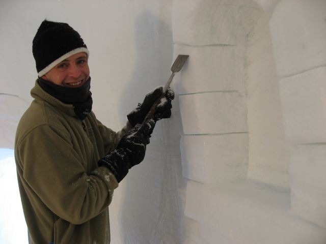 Ice sculptor using specialized tools to carve a large ice wall block indoors