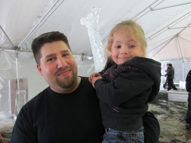Proud father holding his young daughter next to a clear ice sculpture