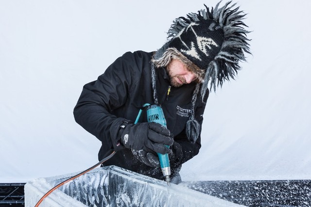 Close up of an ice sculptor using a precision power drill tool on a clear ice block