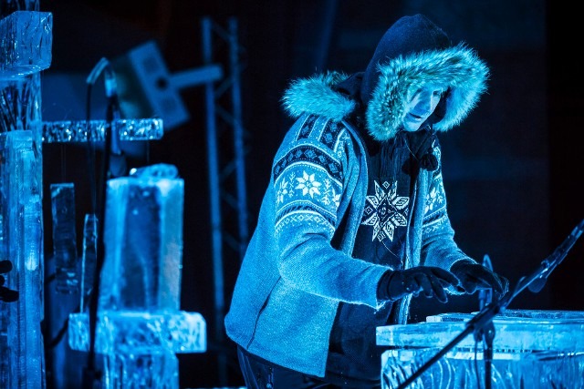 Professional ice carver heavily bundled up in winter gear shaping a clear ice block