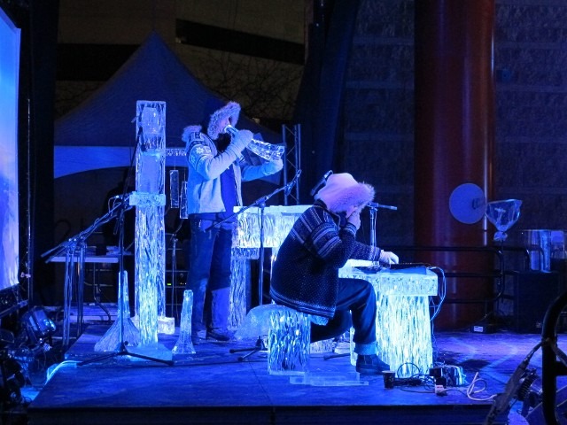 Live band musicians performing on an outdoor winter festival stage under deep blue light