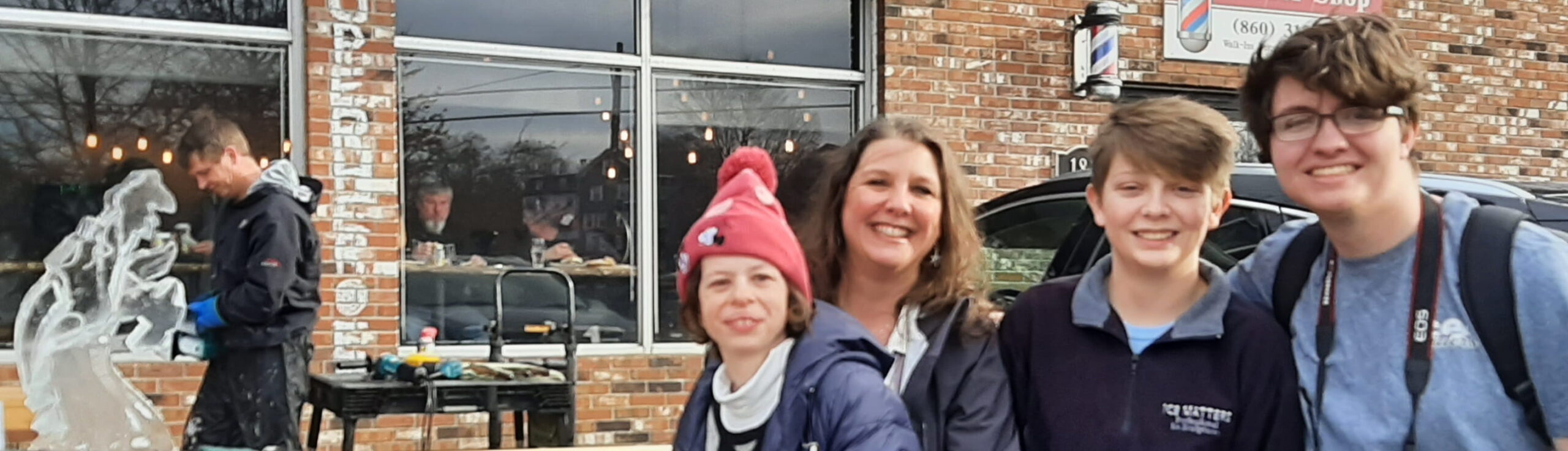 Family posing happily outdoors next to an event ice sculpture display