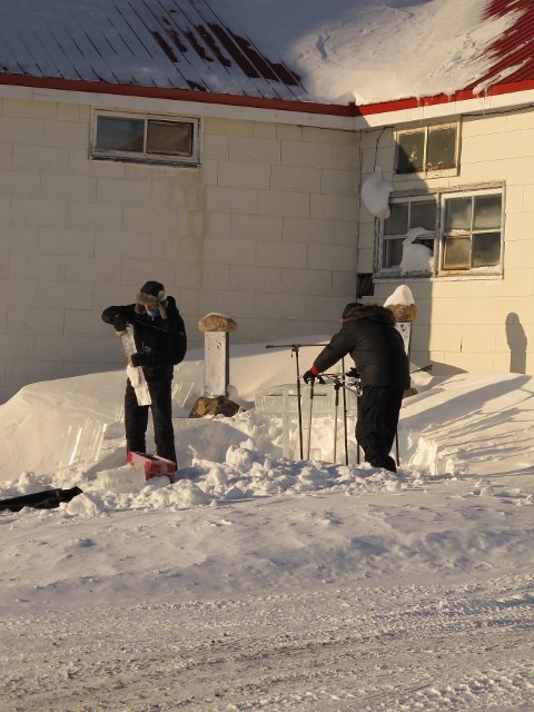Worker shoveling heavy snow accumulation next to an outdoor event building