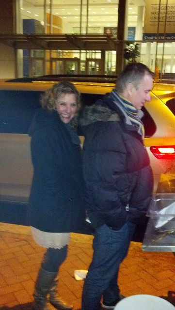 A man and woman smiling together next to a yellow vehicle at an evening function