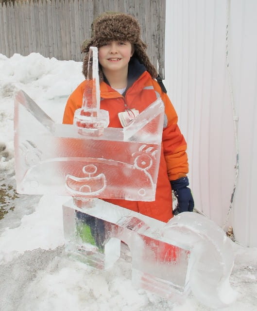Young girl in a winter jacket posing with a decorative ice carving display