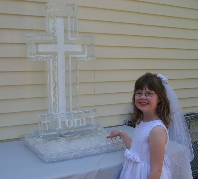 Young girl wearing a veil posing next to an elegant church cross ice carving