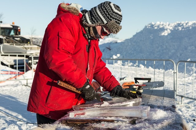 Artisan using a handheld chainsaw to shape an outdoor winter ice installation
