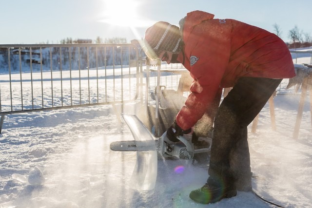 Sculptor carefully cutting a precise line into an outdoor ice block