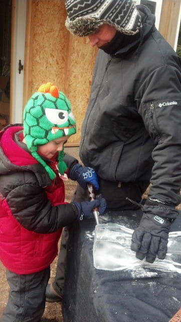 Young child wearing a green knitted monster hat looking at an outdoor display