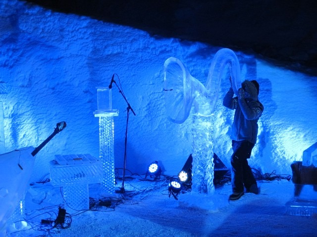 Musicians performing live with acoustic instruments inside a glowing blue ice room
