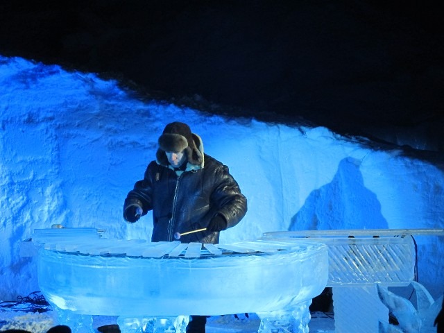 Person inspecting a carved out ice room cavern illuminated in cold blue light