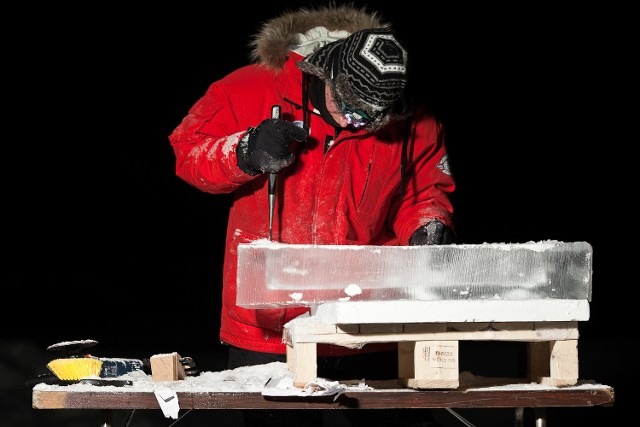 Ice carver in a red heavy winter jacket prepping a clear ice block