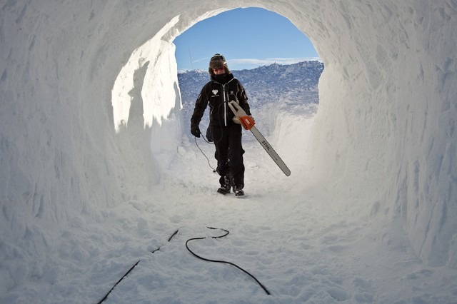 Person walking through a perfectly round carved ice tunnel exit