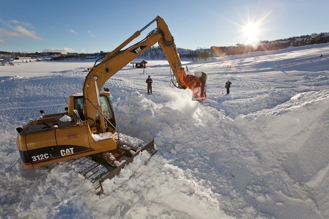 Construction vehicle moving snow and large ice blocks at an outdoor site