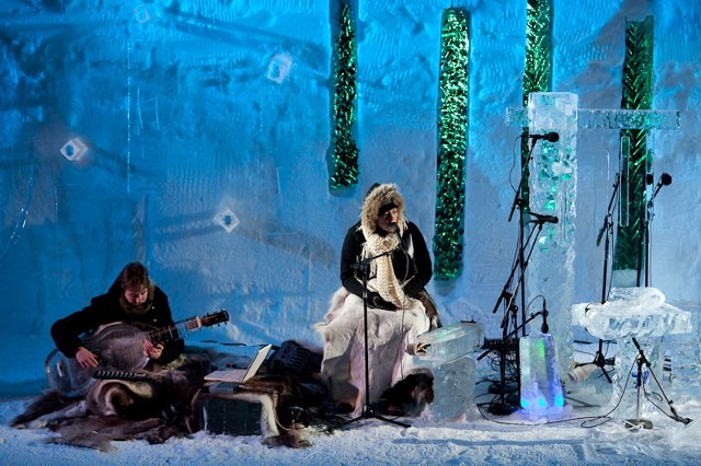 Musician performing with an instrument inside an illuminated ice palace hall