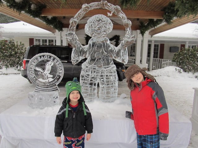 Ornate ice sculpture of a figure or angel surrounded by event attendees outdoors