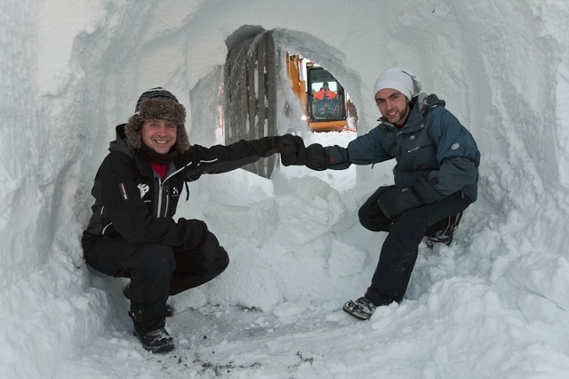 Two people inside a snow fort or ice cave building an internal structure