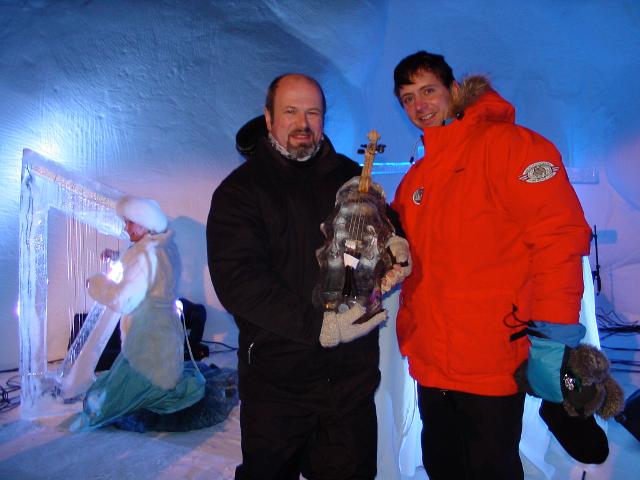 Two event team members in winter coats posing next to a finished ice sculpture