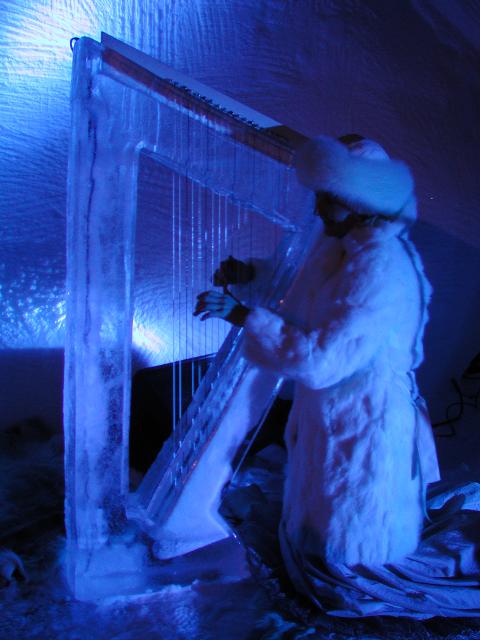 Person carving fine details into a massive ice wall glowing with blue light